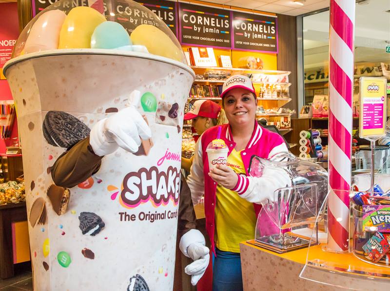Jamin-Shaker-Mascotte-in-Actie-bij-Jamin-2 Individuelles Produktmaskottchen-Kostüm in Form eines Getränks vor einem Milchshake-Laden.